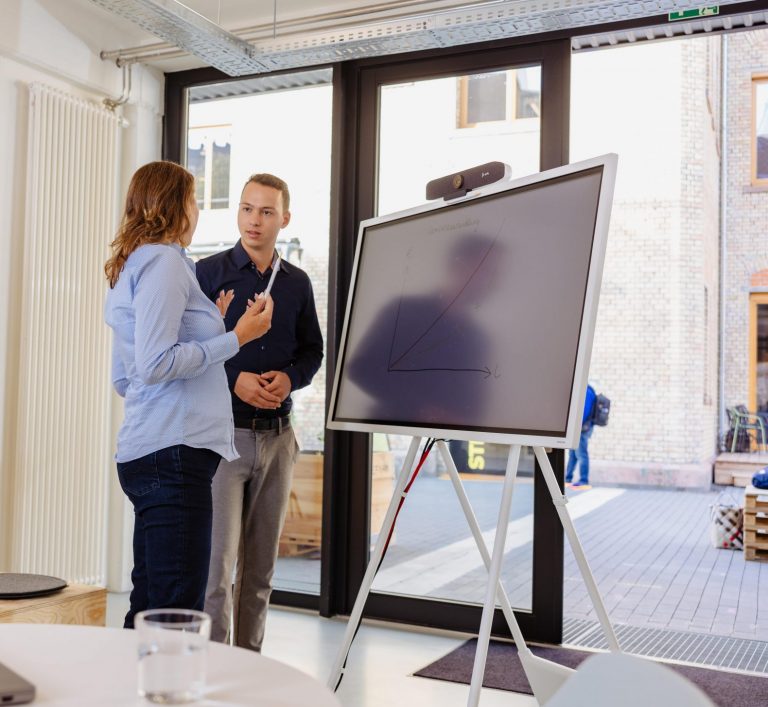 Coaching-Situation mit zwei Personen vor einem digitalen Whiteboard in einem modernen Büro.